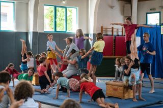 Viele Kinder machen Partnerkrobatik in einer Turnhalle.